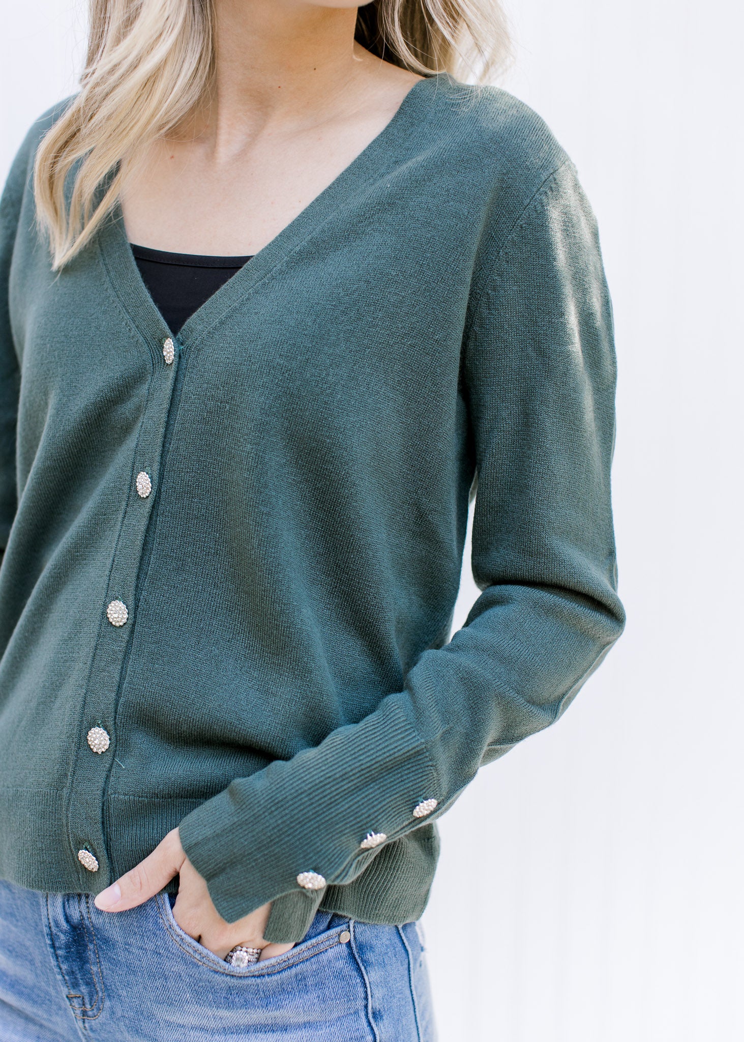 Close up of flower rhinestone buttons closure and cuff detail on a green long sleeve cardigan. 