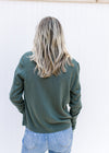 Back view of Model wearing a green long sleeve cardigan with slightly cropped fit and button closure