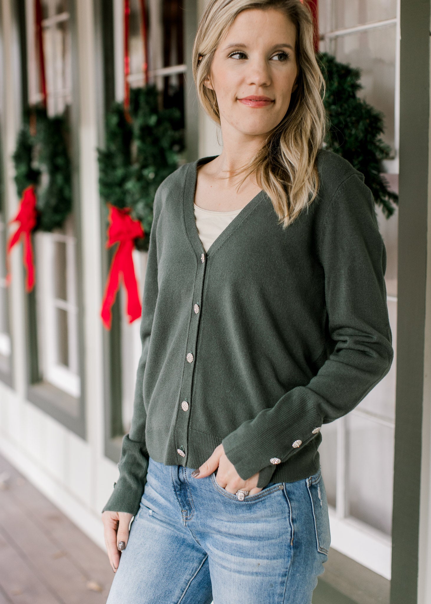 Model wearing a green long sleeve cardigan with flower rhinestone button closure and cuff detail. 