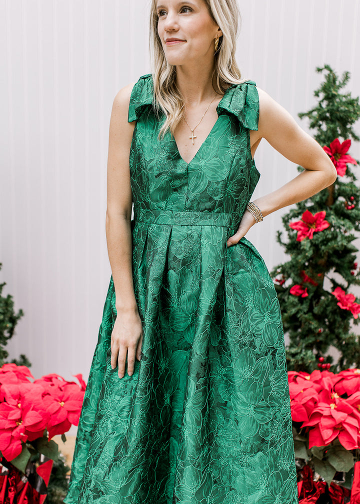 Model wearing a bright green sleeveless midi with embroidered floral, pleated waist and a v-neck. 