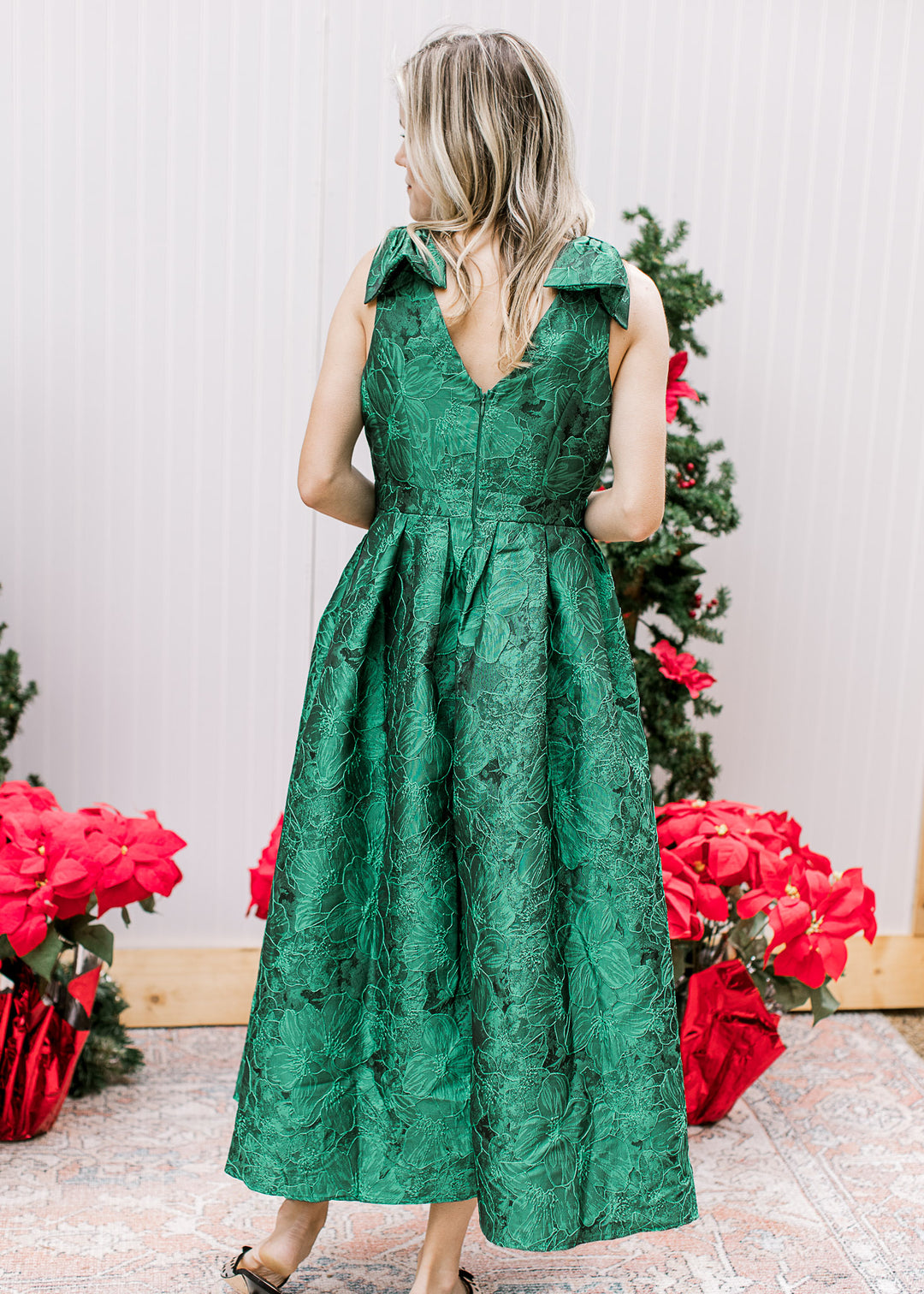 Back view of Model wearing a bright green midi with embroidered floral, pleated waist and a v-neck. 