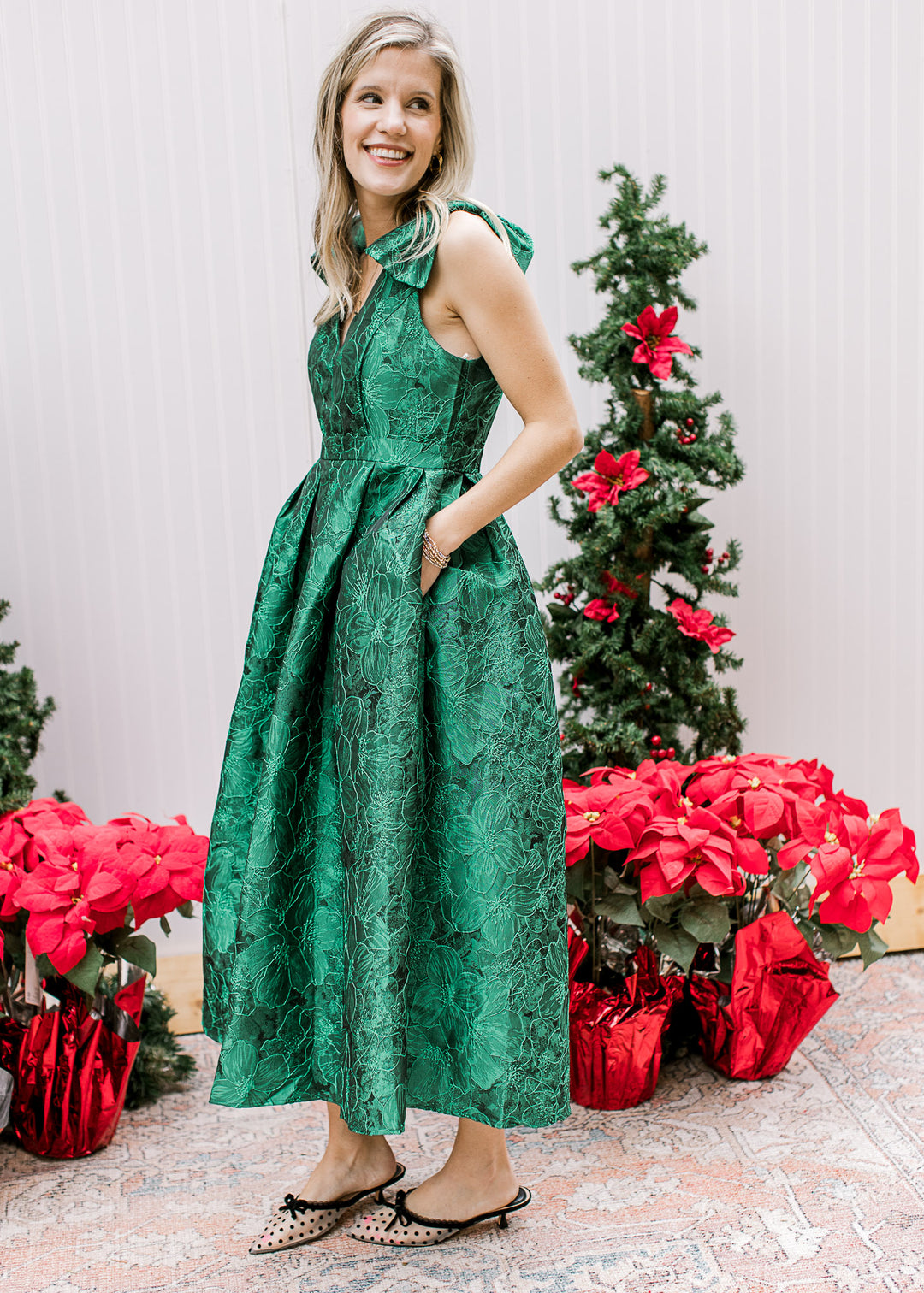 Model wearing low heels and a bright green midi with embroidered floral, pleated waist and a v-neck.