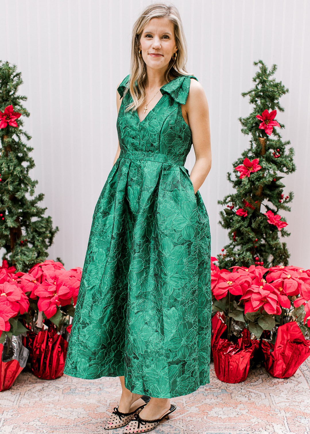 Model wearing a bright green midi with embroidered floral, pockets and bows at the shoulder. 