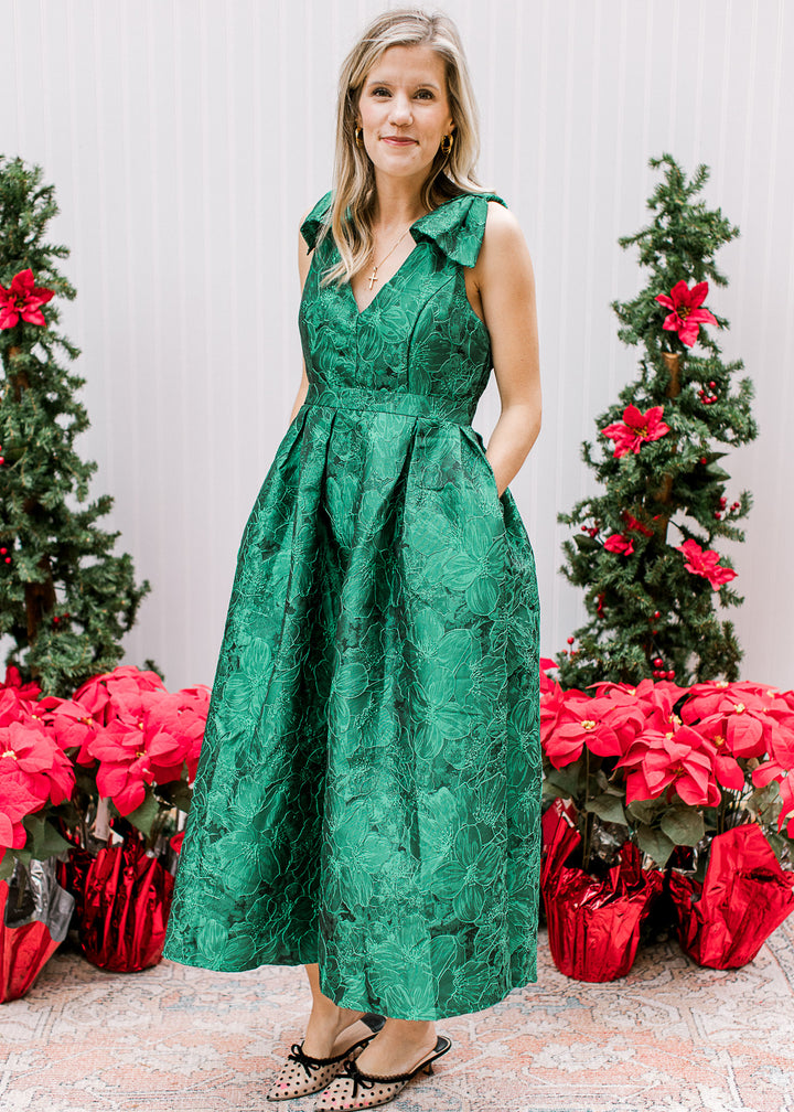 Model wearing a bright green midi with embroidered floral, pockets and bows at the shoulder. 