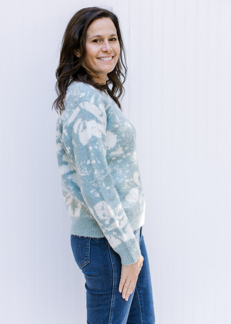 Model wearing a sage sweater with a cream design, long sleeves, a crew neck and acrylic material. 