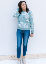 Model wearing jeans, mules and a sage sweater with a cream design, long sleeves, and a crew neck.