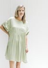 Model wearing a green above the knee dress with a patch pocket, cuff short sleeves. 