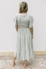 Back view of Model wearing a pale green maxi with a smocked bodice, short sleeves and a v-neck.