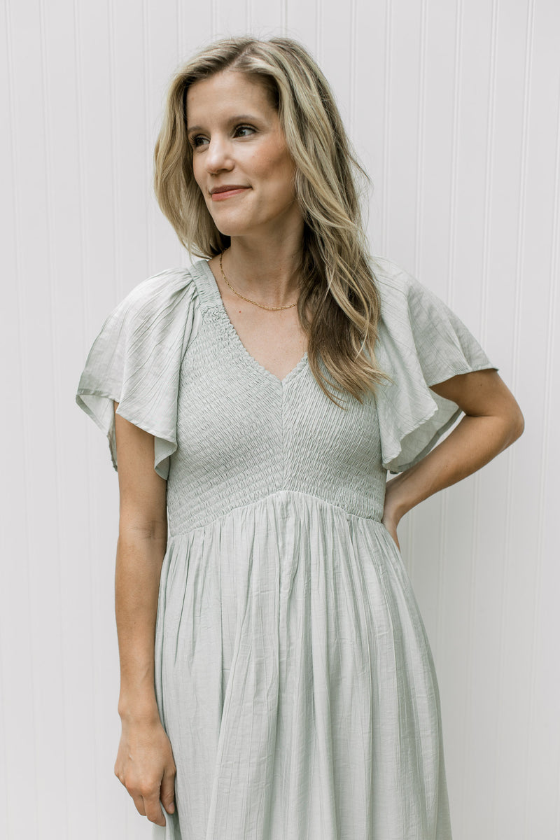 Close up of smocked bust, flutter short sleeves and a v-neck on a pale green maxi.