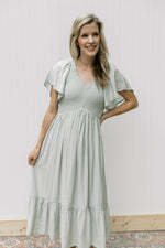 Model wearing a pale green maxi with a smocked bodice, flutter short sleeves and pockets.