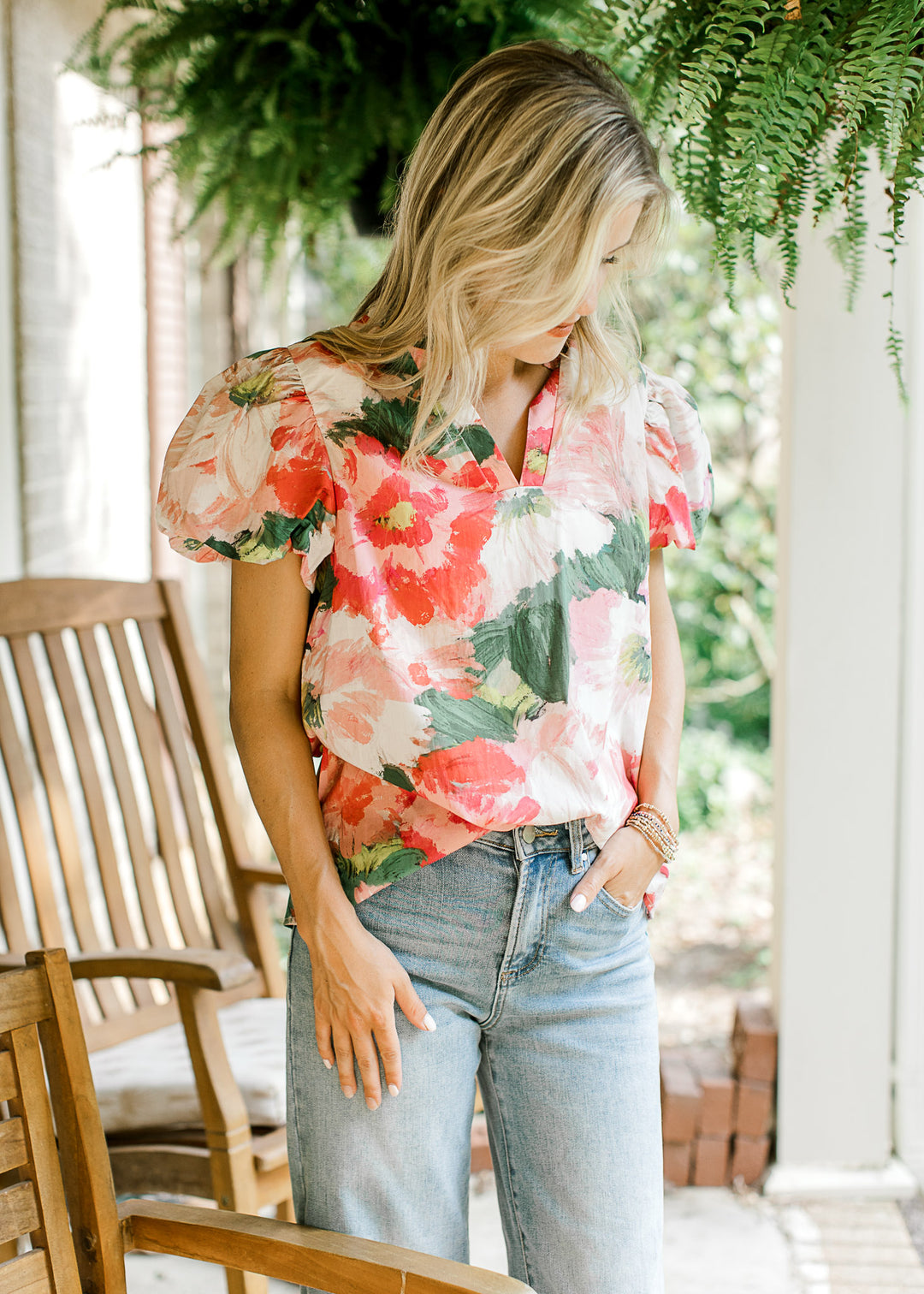 Model wearing a cream top with pink and green floral, short bubble sleeves and v-neck with ruffle.