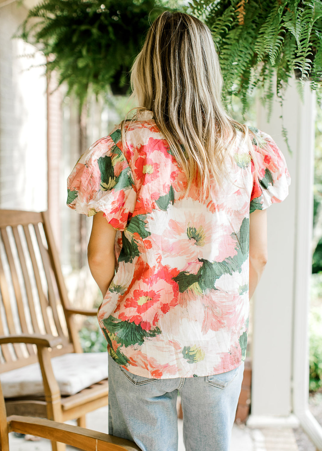 Back view of Model wearing a watercolor floral top with short bubble sleeves and v-neck with ruffle.
