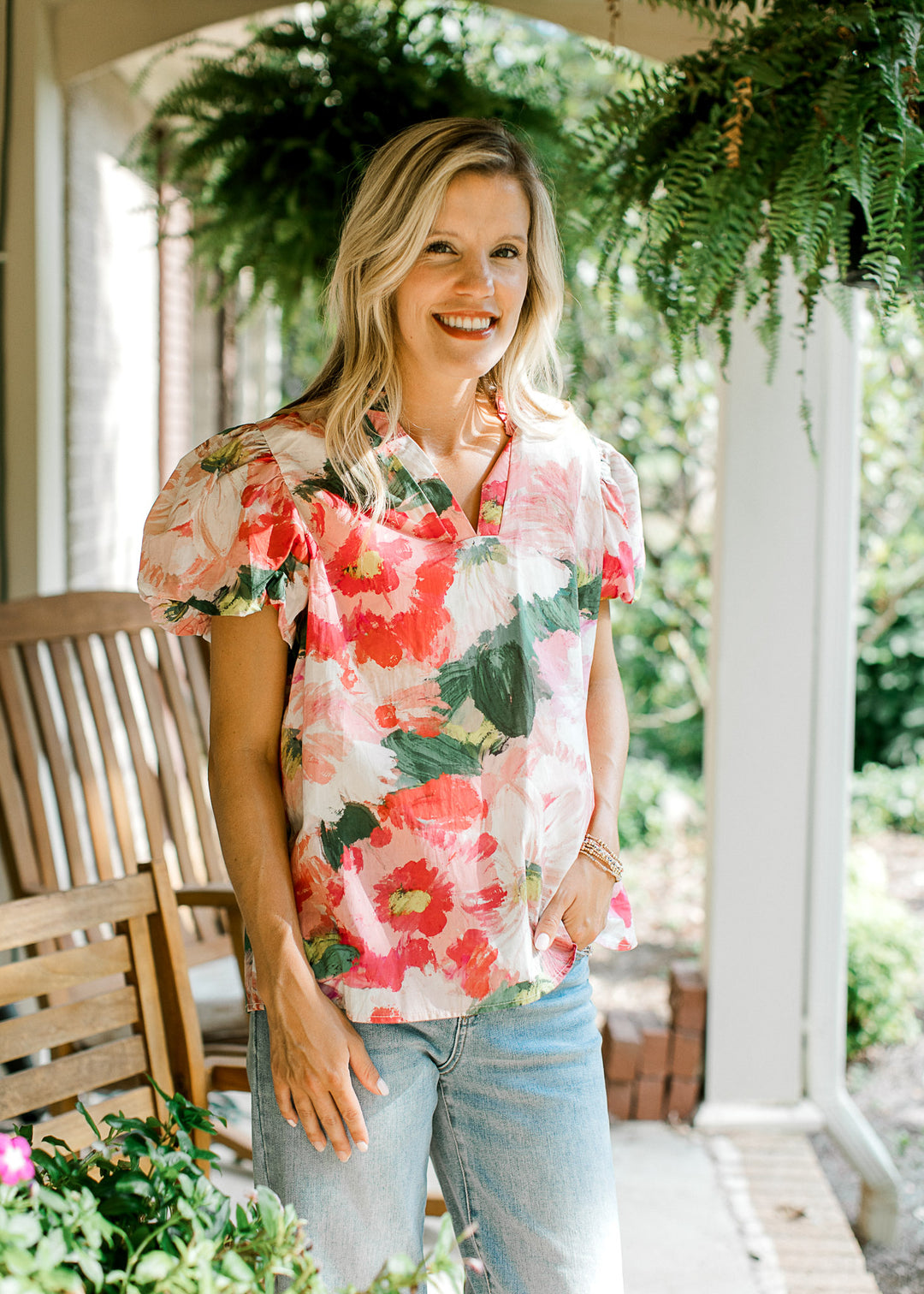 Model wearing jeans and a watercolor floral  top with short bubble sleeves and v-neck with ruffle.