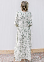 Back view of model wearing a beige maxi with sage flowers and long sleeves. 