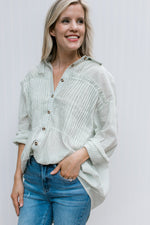 Model wearing a cream button up top with green pinstripes, long sleeves and ruffle at bust.