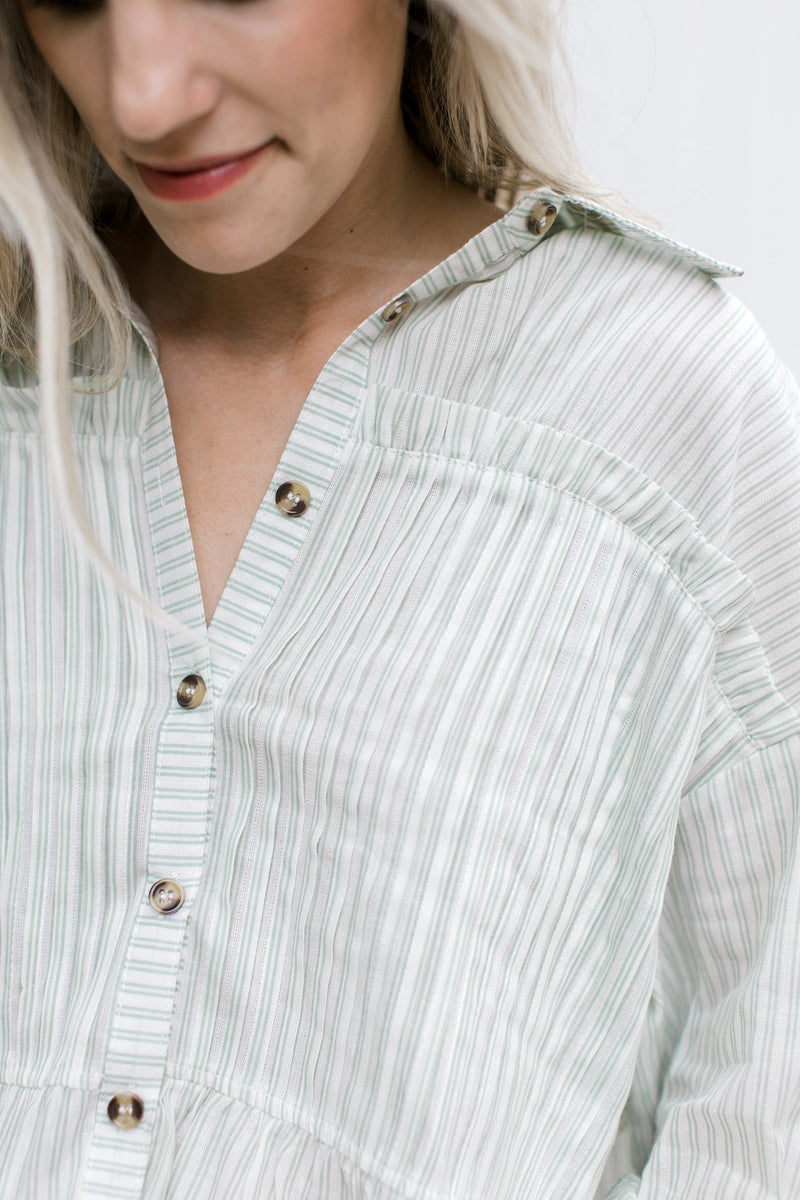 Close up of ruffle detail across the bust of a cream button up top with green pinstripes.