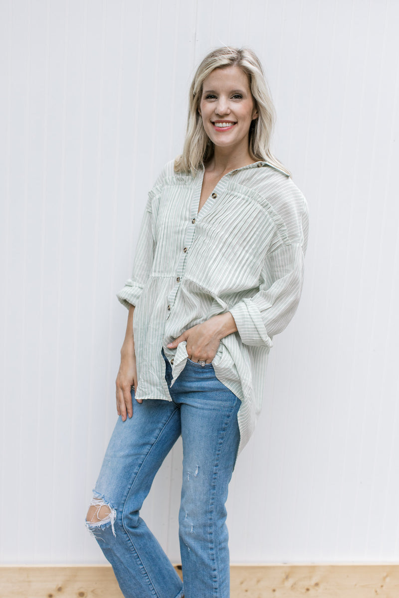 Model wearing jeans and a cream button up top with green pinstripes and long sleeves