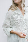 Close up of pleating on the front of a cream button up top with green pinstripes.