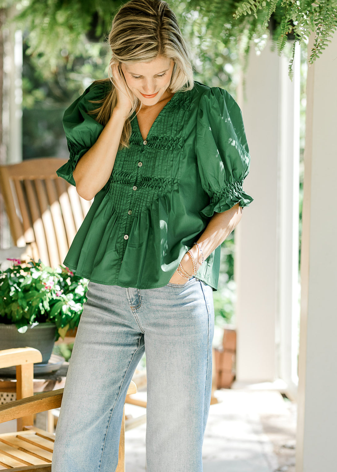 Model wearing jeans and a green blouse with a pleated front, bubble short sleeves and button front. 