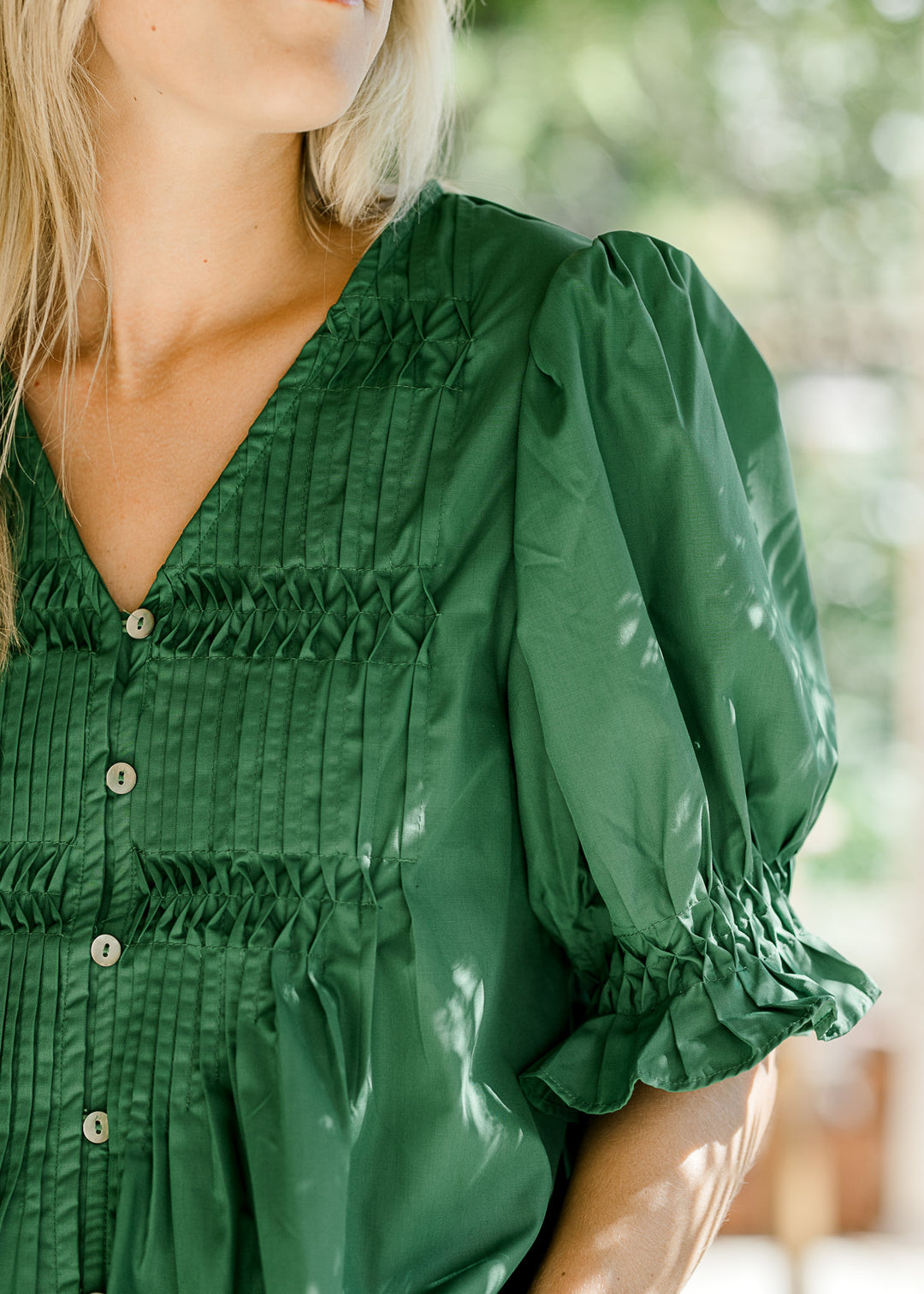 Model wearing a green blouse with a pleated front, bubble short sleeves and button front. 