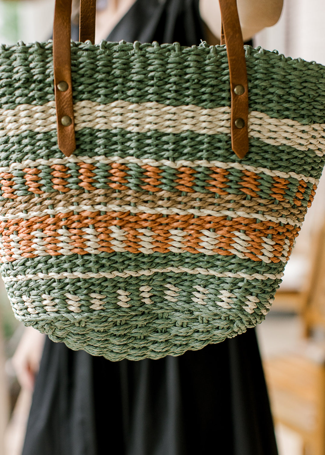 Close up of taupe, cream, green, and rust woven purse with a faux leather straps and a pocket. 