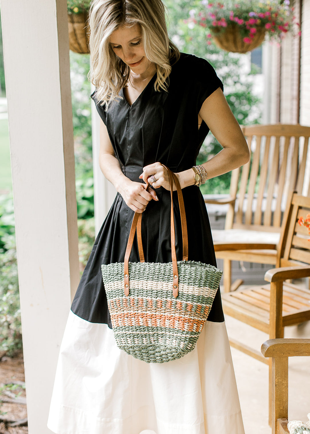 Model holding a woven purse with taupe, cream, green, and rust pattern a faux leather straps.