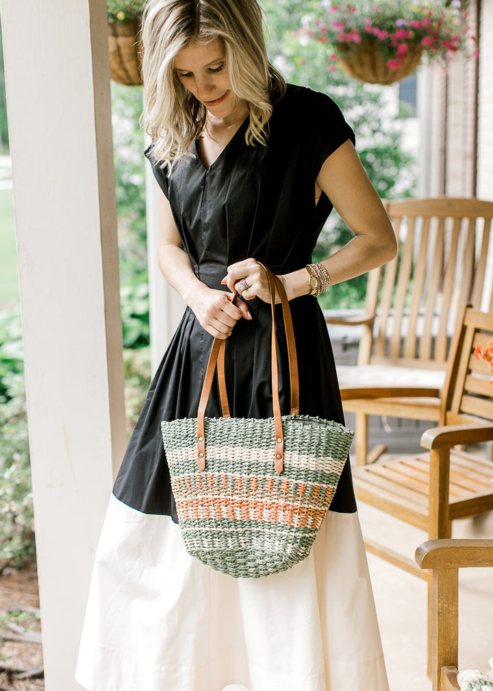 Model holding a woven purse with taupe, cream, green, and rust pattern a faux leather straps.