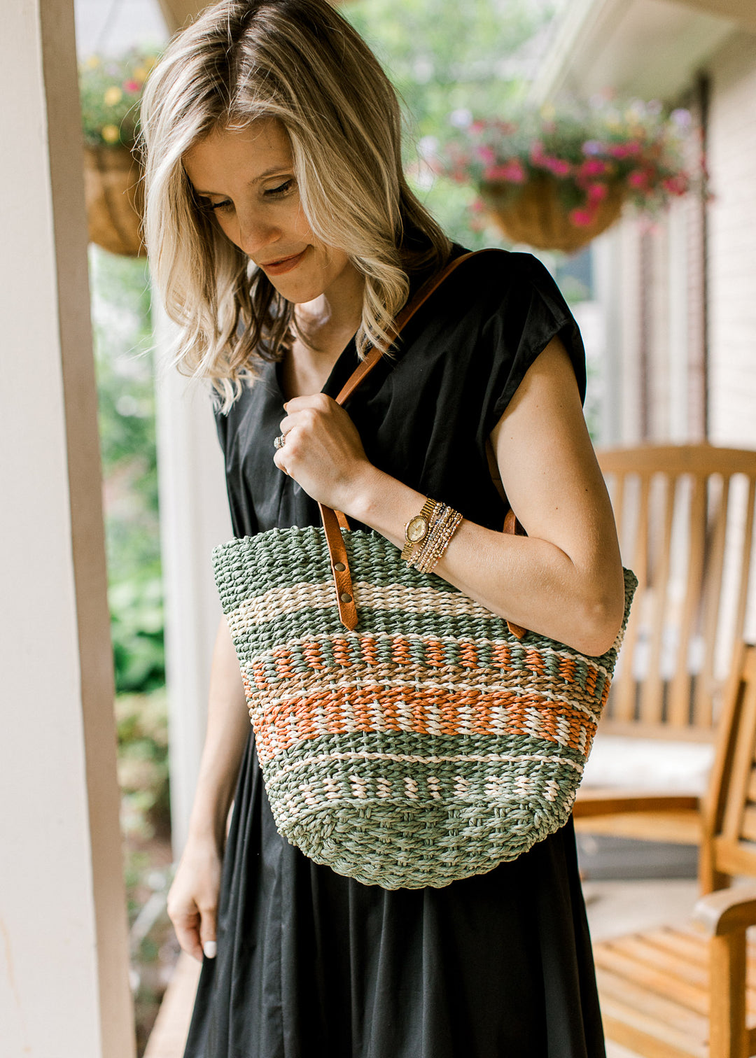 Model with a woven straw purse with taupe, cream, green, and rust pattern a faux leather straps.