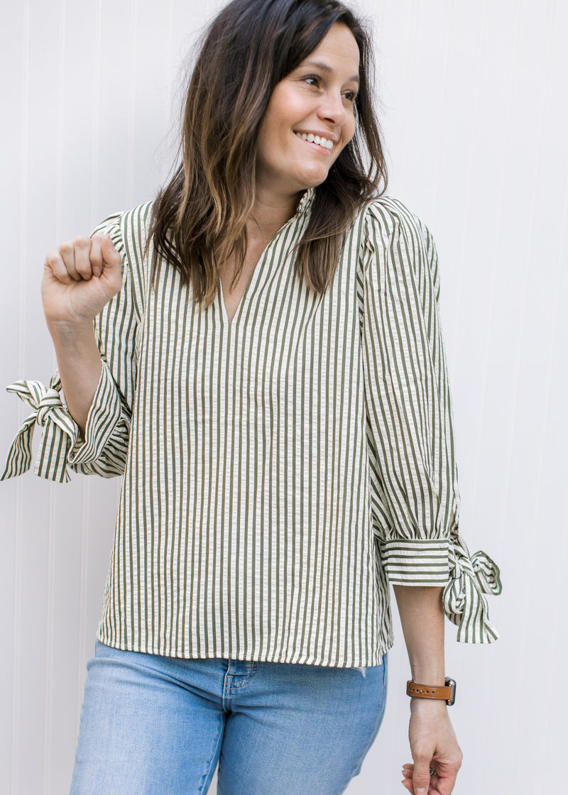 Model wearing jeans and a cream top with green stripes, ruffle at neck and tie at cuff of 3/4 sleeve