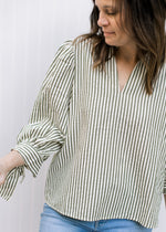 Model wearing a cream v-neck top with green stripes, pleated shoulders and 3/4 sleeve.