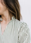 Close up of pleated shoulder and ruffle at neck of a cream top with green stripes. 