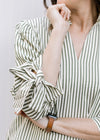 Close up of tie at cuff of 3/4 sleeve on cream top with green stripes, v-neck and pleated shoulder.