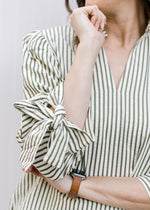 Close up of tie at cuff of 3/4 sleeve on cream top with green stripes, v-neck and pleated shoulder.