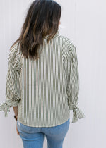 Back view of Model wearing a cream top with green stripes and 3/4 sleeve with tie at cuff.