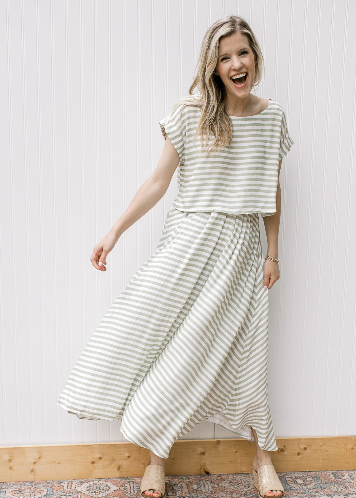 Model wearing wedges and a green and white striped set with a boatneck top and flowy skirt. 