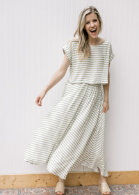 Model wearing wedges and a green and white striped set with a boatneck top and flowy skirt. 