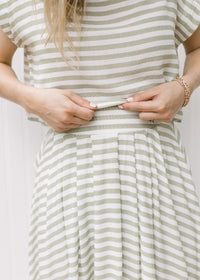 Close up of pleating at the top of a flowy green and white skirt and a cropped top with a boatneck.