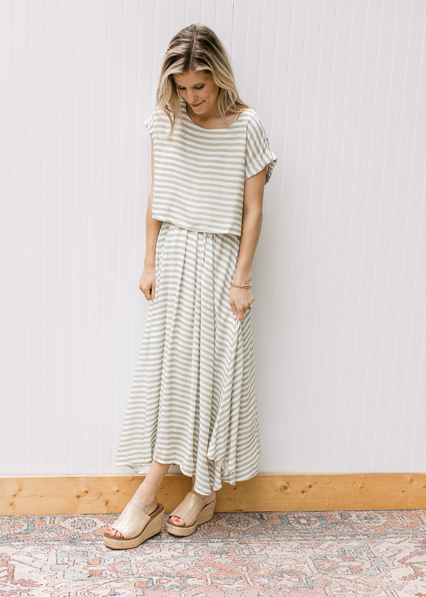Model wearing wedges and a green and white striped set with a cropped top and flowy skirt. 