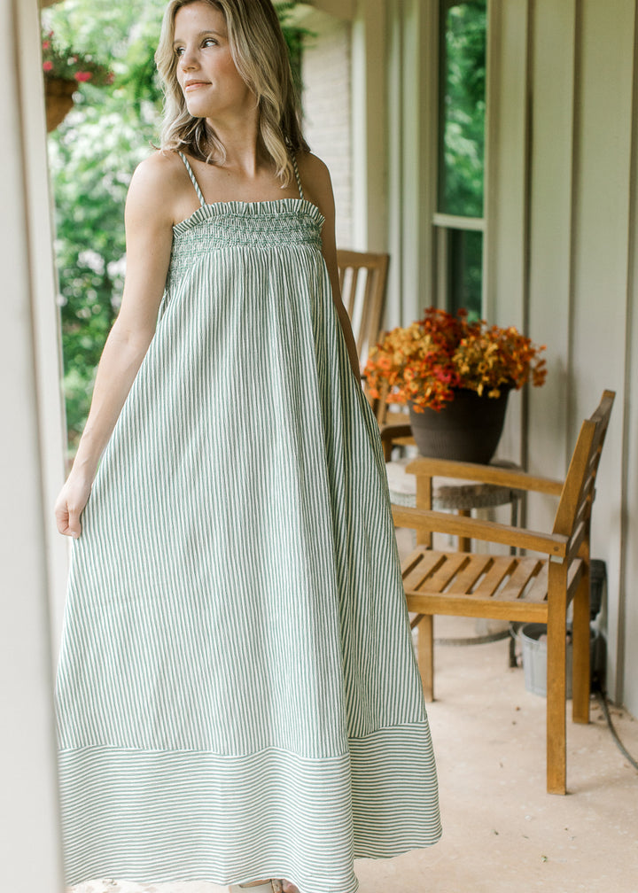 Model wearing a flowy green and cream striped maxi with ruffle on elastic neck and spaghetti straps.