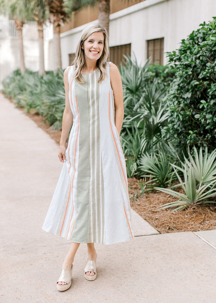 Model wearing wedges and a cream sleeveless midi with a varied green stripe pattern and round neck. 