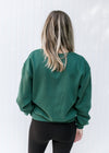 Back view of Model wearing a deep green sweatshirt with a round neck and an embroidered lego.