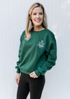 Model wearing a deep green sweatshirt with a round neck and an embroidered white logo. 