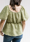 Back view of a model wearing an avocado v-neck top with bubble short sleeves and elastic waist. 