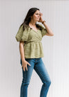 Model wearing a avocado green v-neck top with a pleated wave texture and short bubble sleeves. 
