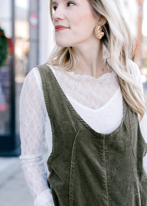 Close up of corduroy material on an olive green jumpsuit over a white lace long sleeve top. 