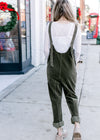 Back view of an olive colored corduroy jumpsuit with adjustable straps over a white lace top.