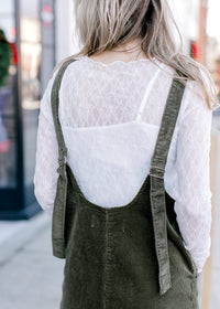 Back view of Model wearing a long sleeve lace top with a spaghetti strap undershirt and boat neck.