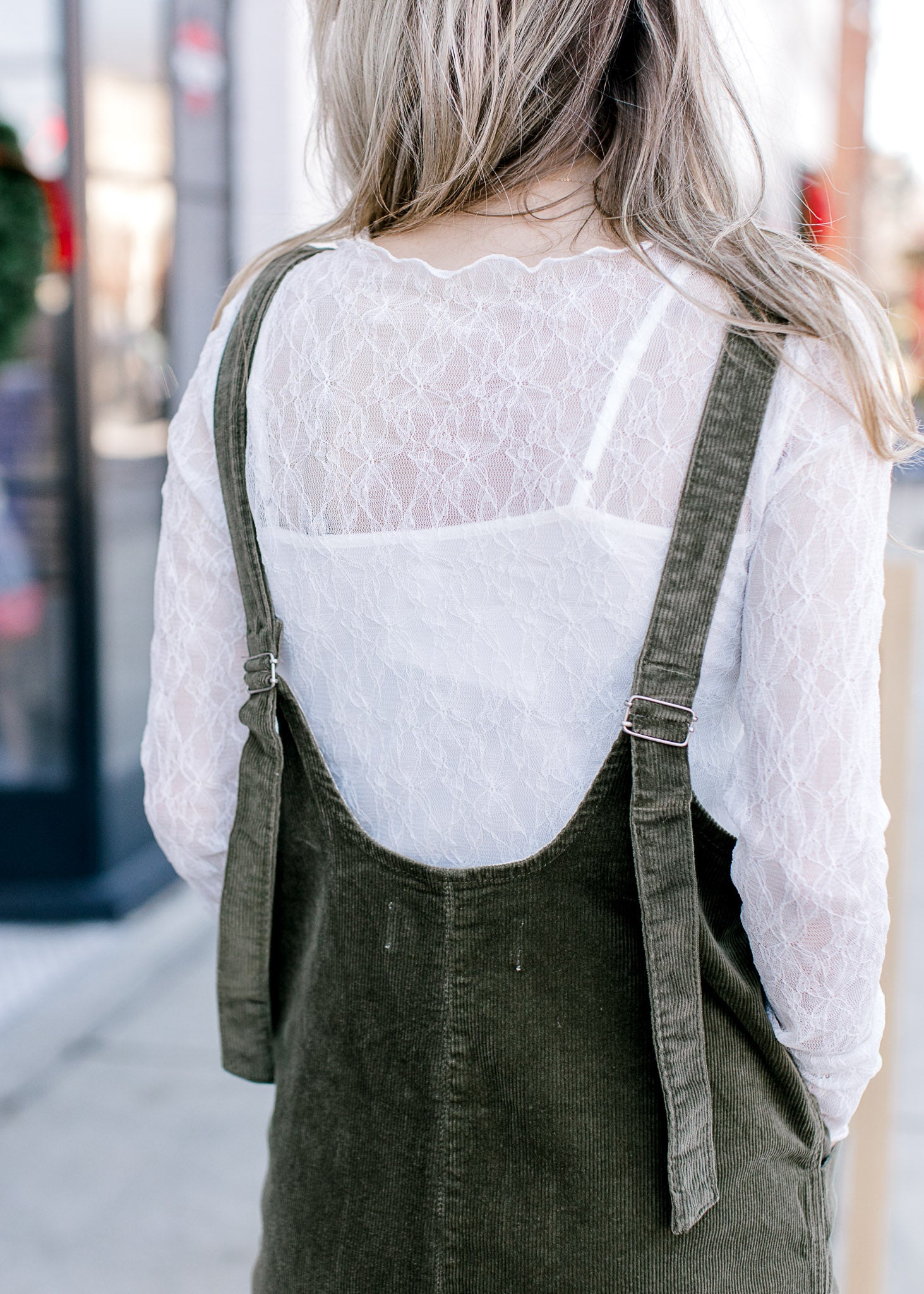 Back view of Model wearing a long sleeve lace top with a spaghetti strap undershirt and boat neck.