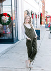 Model wearing mules with a long sleeve lace top over an olive corduroy jumpsuit. 