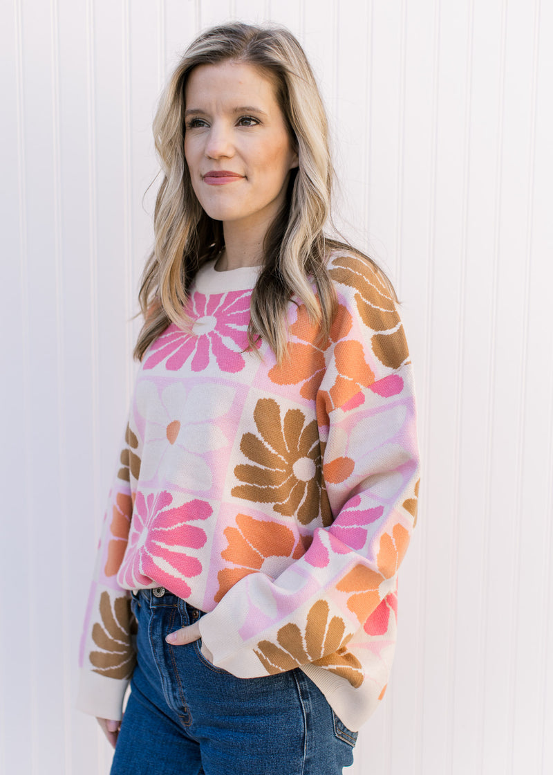 Model wearing a cream sweater with oversized orange, pink, rust and taupe flowers and a round neck.